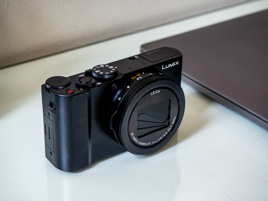 Photo: A black camera on a white glass surface next to a gray laptop