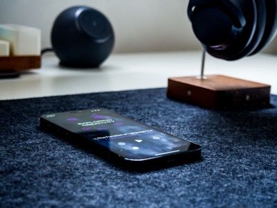 Phone on Desk with Headphones and Podcast - A smartphone and headphones on a desk mat