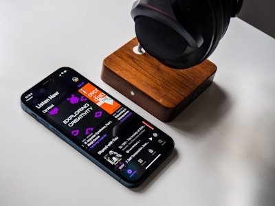 Phone with Podcast and Headphones on White Desk - A smartphone and headphones on a white desk