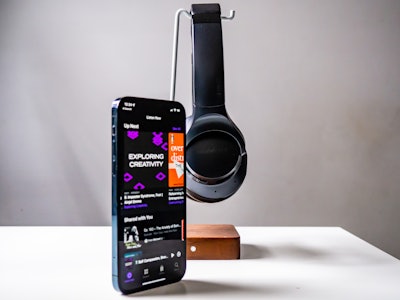 Headphones with Phone and Podcast on White Desk - A phone and headphones on a stand