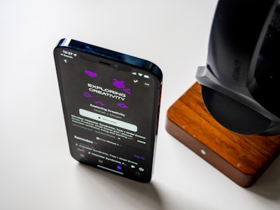 Phone and Headphones on Desk - A smartphone with a podcast playing next to headphones on a stand