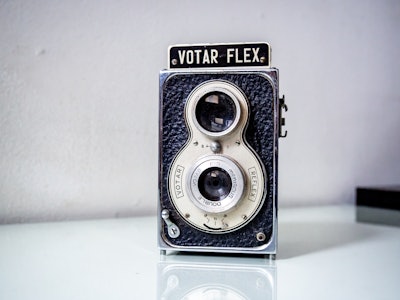 Vintage Camera on Desk - A vintage metal black and gray camera on a white glass table surface 