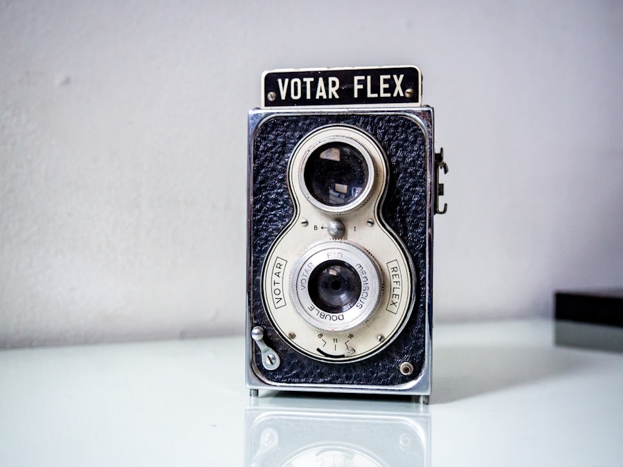 Photo: A vintage metal black and gray camera on a white glass table surface 