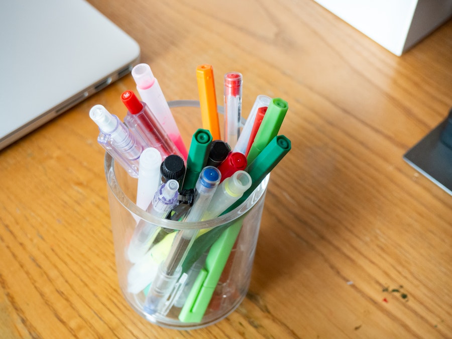 Photo: A cup full of pens, markers, pencils, and highlighters on a wooden desk next to a laptop