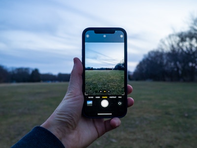 Hand Holding iPhone Taking Photo - A hand holding a smartphone while taking a photo of a field of grass