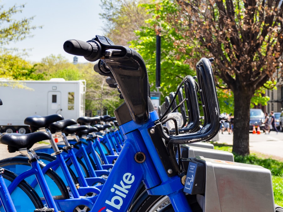 Photo: A row of blue bicycles in front of a white trailer outside a park