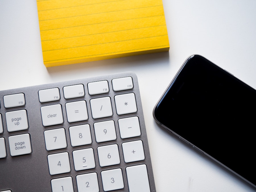 Photo: Keyboard, Phone, and Yellow Note on White Desk