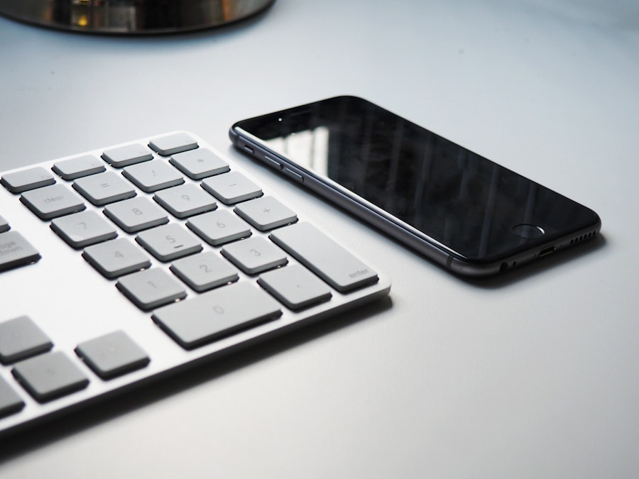 Photo: A keyboard and a smartphone on a white desk. Black, gray, and white color palette 