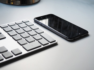 Keyboard and iPhone on Desk - A keyboard and a smartphone on a white desk. Black, gray, and white color palette 