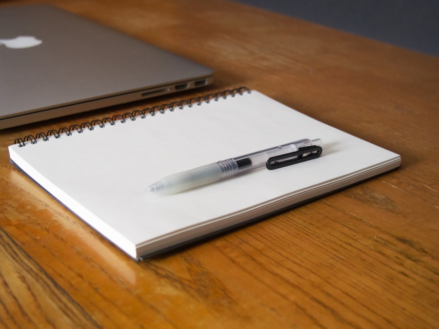 Photo: A notebook, laptop, and pen on a wooden table