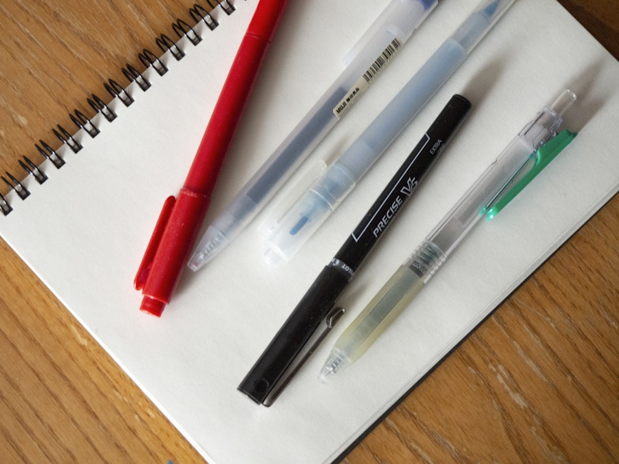 Photo: A group of pens and markers on a notebook sitting on a wooden desk