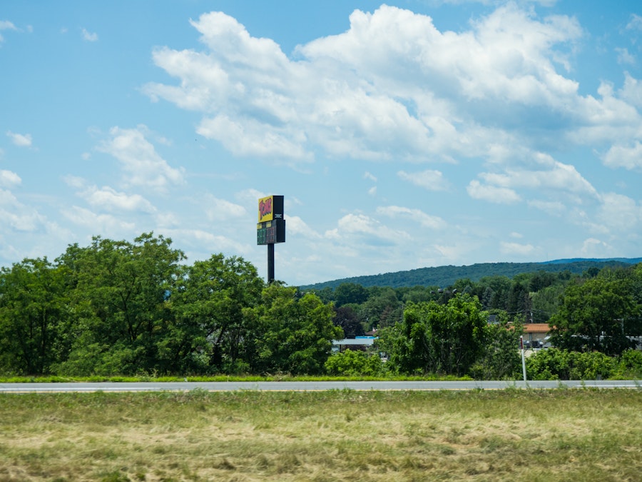 Photo: A field of grass with a sign on a pole and a road in the background