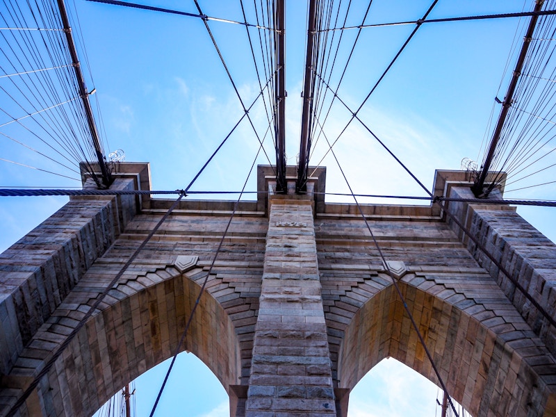 Photo: Looking up at the Brooklyn Bridge with many cables under blue sky and clouds