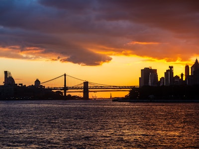 Brooklyn Bridge Sunset - A bridge over water with a vivid yellow and orange sunset and city skyline in the background