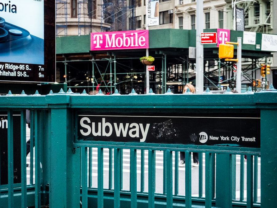 Photo: Subway entrance stairs with a black sign on a green fence