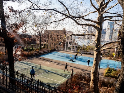 People Playing Pickleball - A group of people playing pickleball in a park with the Manhattan city skyline behind them