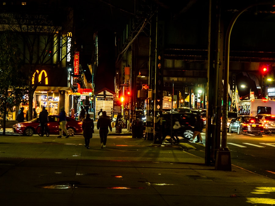 Photo: People walking on a street at night under train tracks