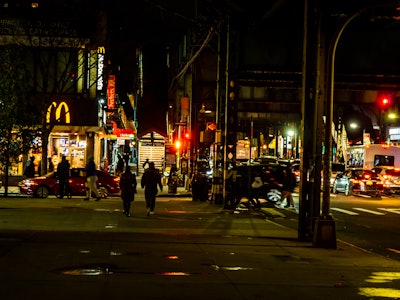 People Walking in Brooklyn at Night - People walking on a street at night under train tracks