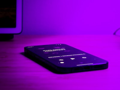 Phone Playing Podcast on Desk - A smartphone on a table under purple lighting 
