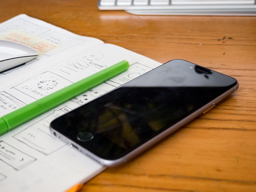 Photo: Phone and Sketchbook on Wooden Desk